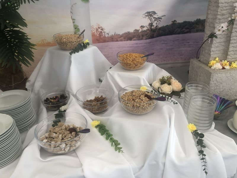 Ein Buffet-Tisch mit Schalen voller Nüsse und Müsli vor einem naturbezogenen Hintergrund, dekoriert mit weißen Rosen und Narzissen.