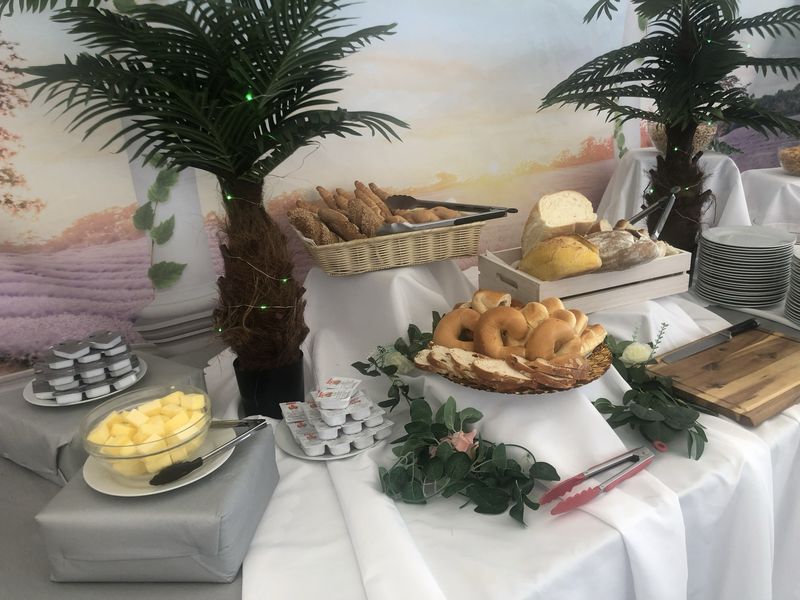 Buffet-Tisch mit verschiedenen Brotsorten, Butter und Tellern, dekoriert mit Palmen und einer malerischen Kulisse.